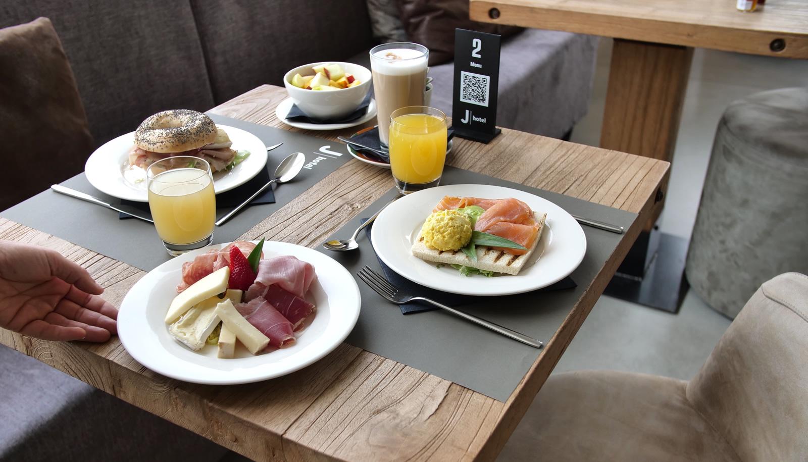 Colazione con bagel, salmone, prosciutto e formaggi, succo d'arancia e cappuccino.