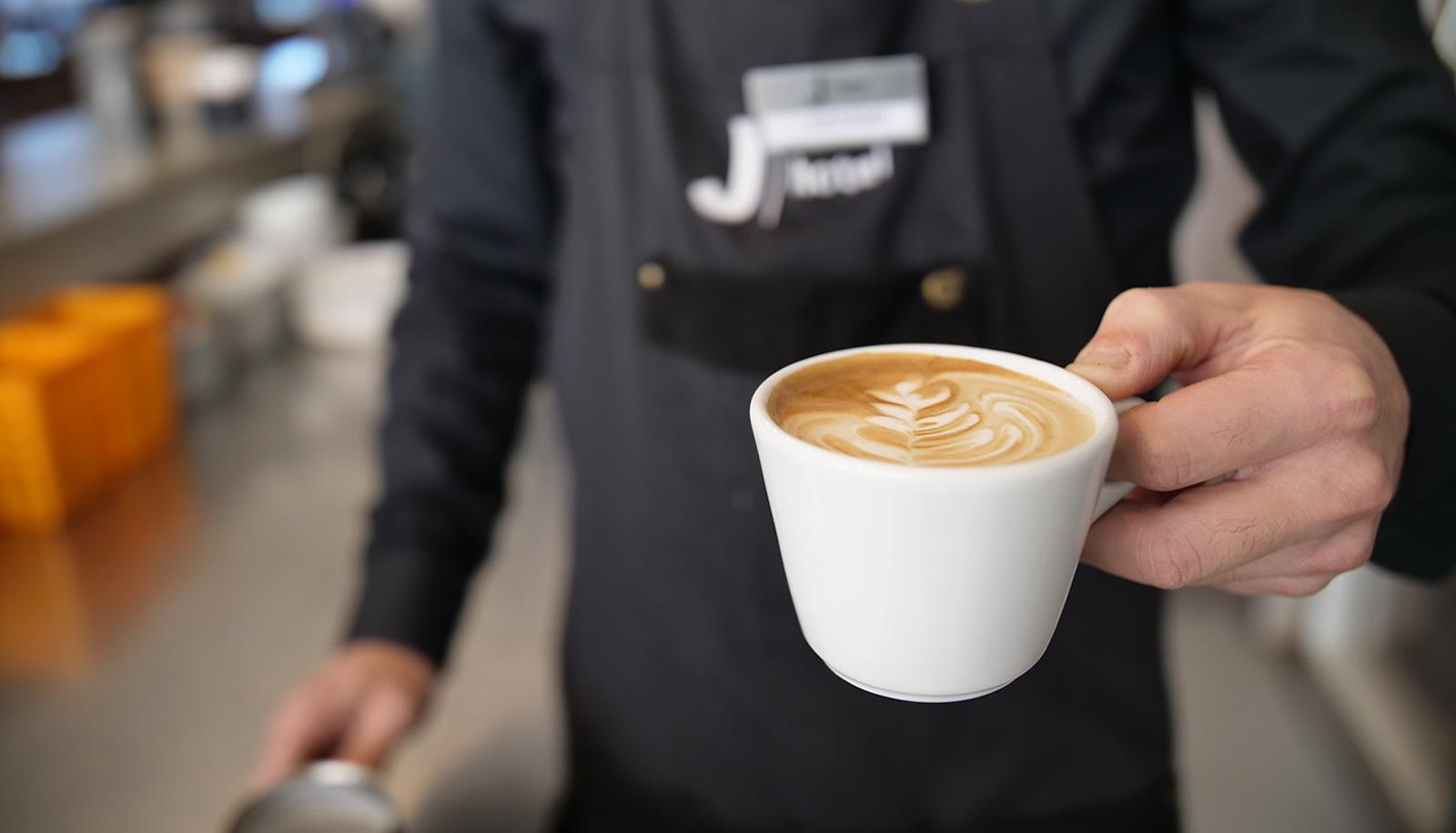 Un barista serve un cappuccino con latte art in una tazza bianca.