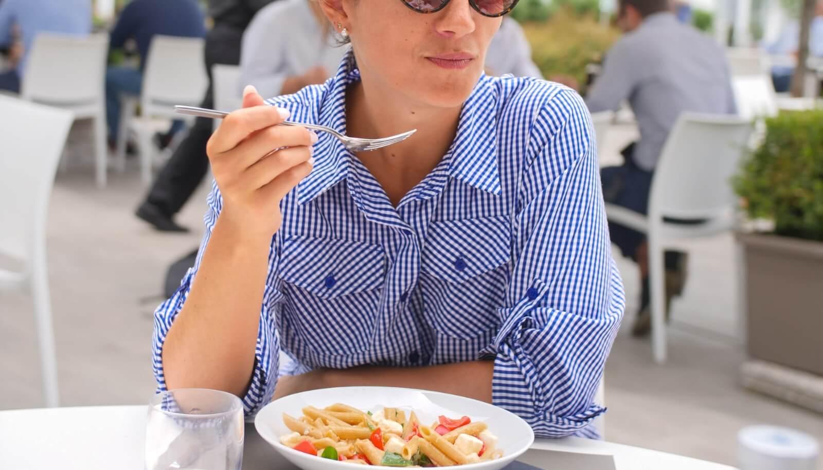 Donna con camicia a righe mangia pasta in un ristorante all'aperto.