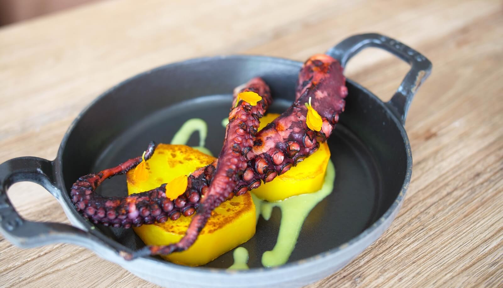 Tentacolo di polpo su patate dorate con salsa verde, servito in padella.