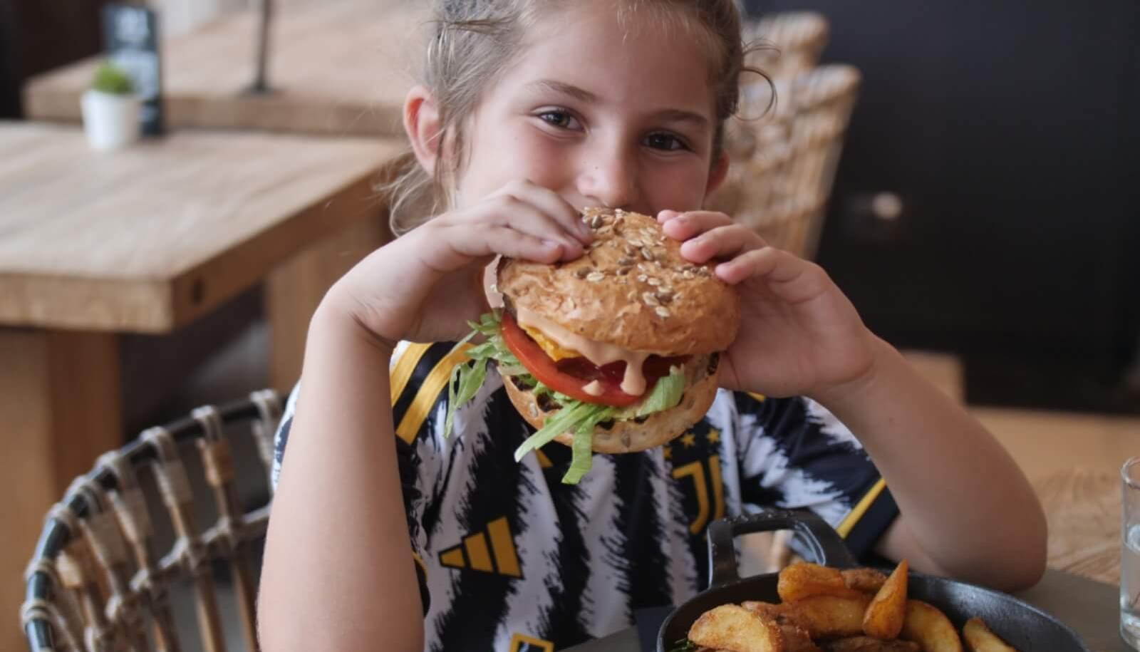 Bambina mangia un hamburger in un ristorante, con patatine fritte nel piatto.